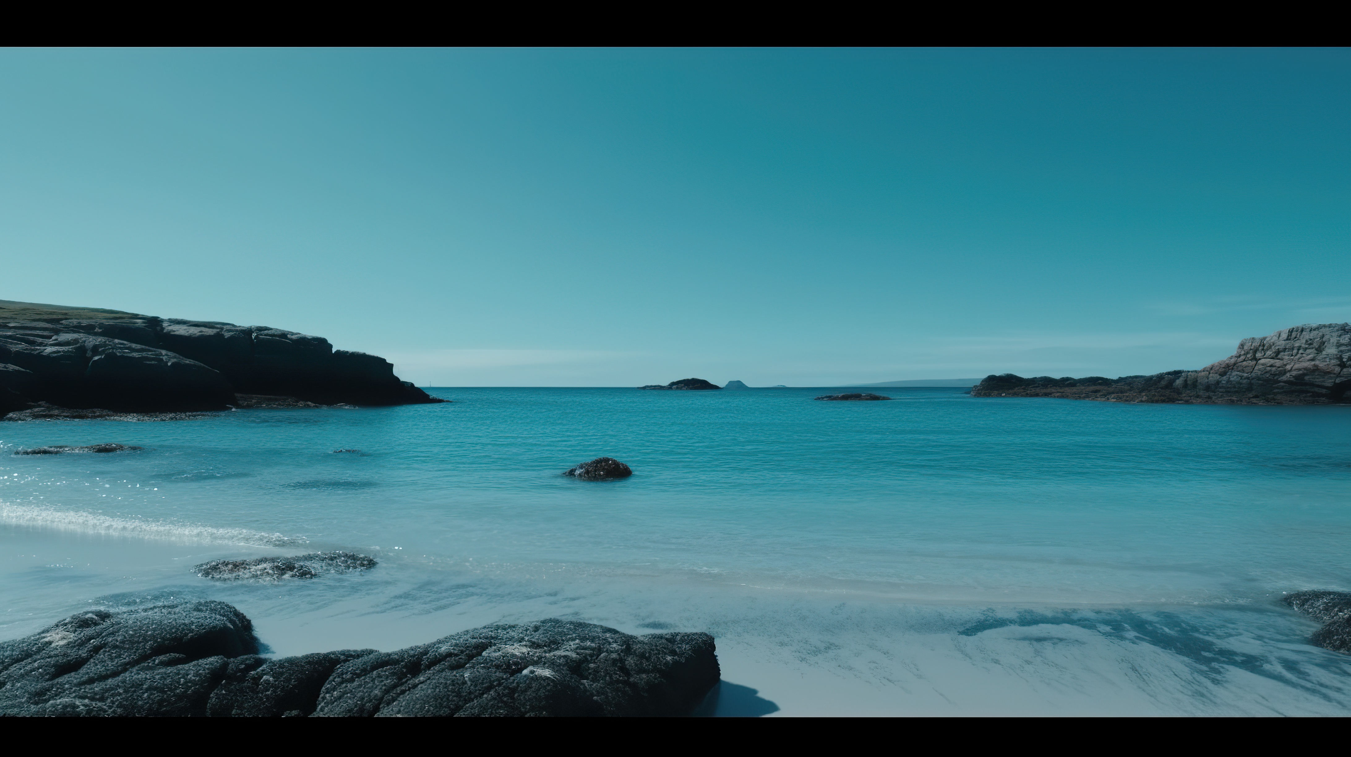 Beautiful blue sky and a beach with clear blue water and rocks on the shore